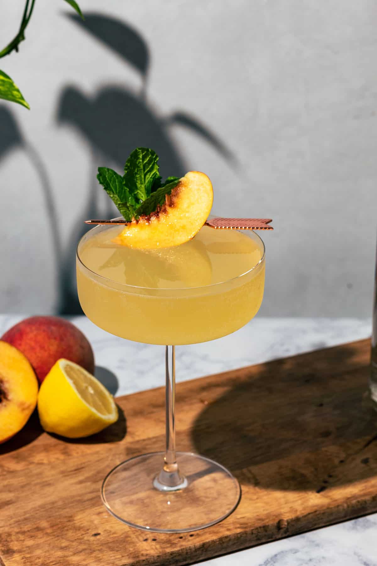 Cocktail in a coupe glass on a wood surface with peach and lemon halves in the background.