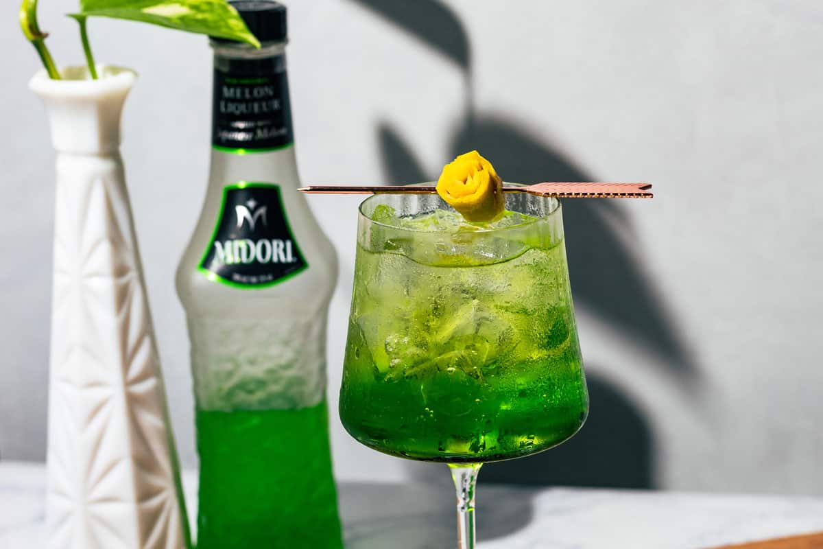 Spritz with a green plant and a bottle of Midori in the background.