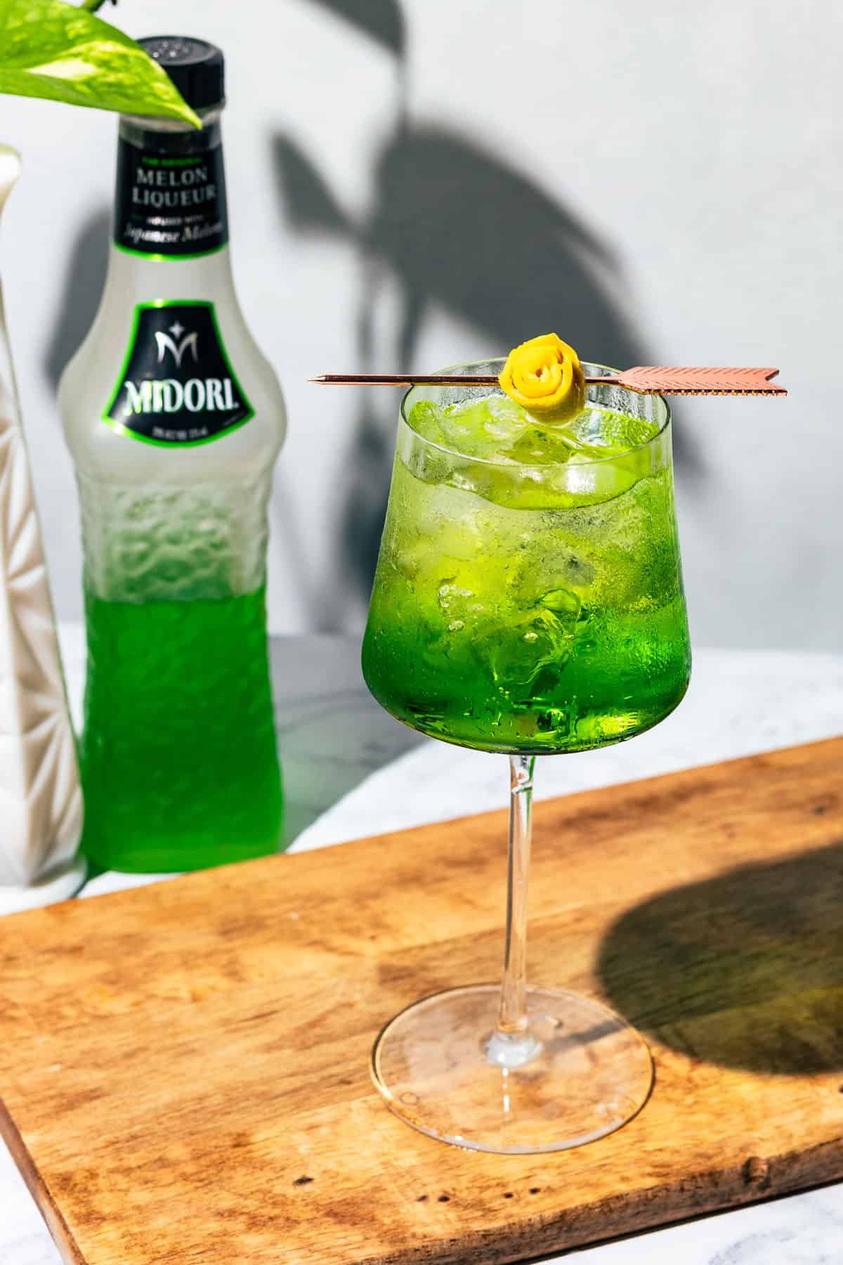 Midori spritz in a wine glass on a wood surface.