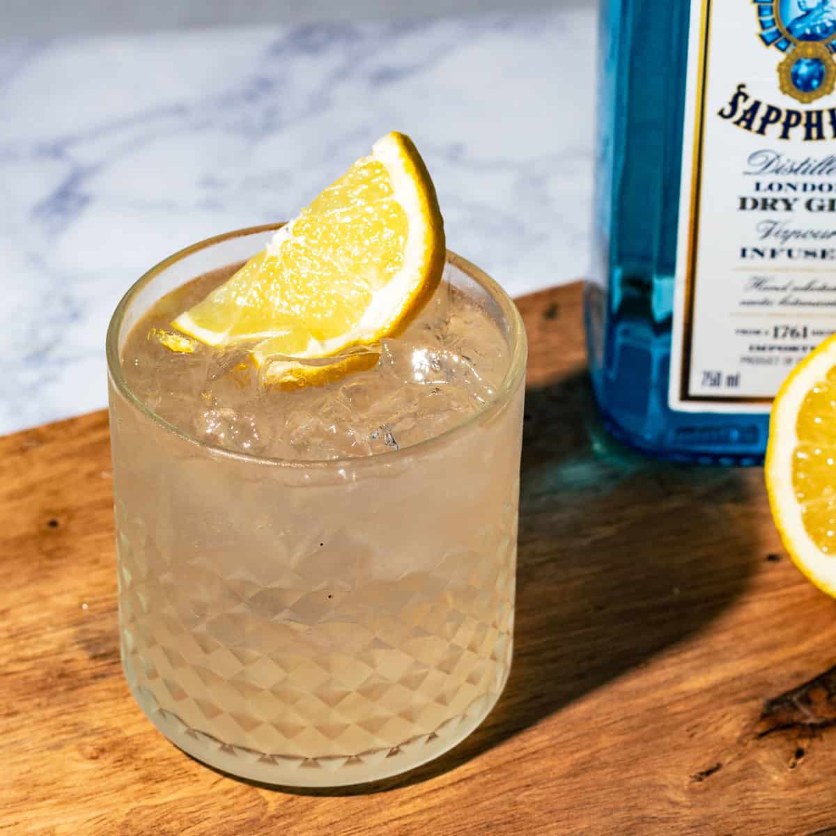 Fitzgerald gin sour garnished with a lemon wedge on wood surface.