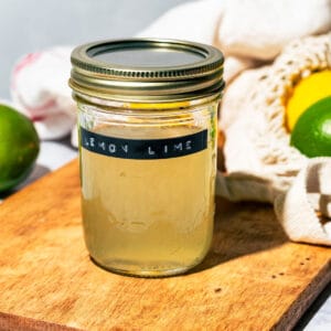 Jar of the syrup on a wood cutting board with lemons and limes scattered around.