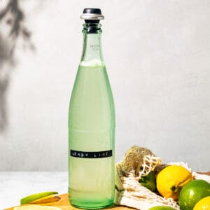Bottle of the soda on a wood board with lemons and limes scattered around.