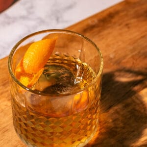 Tequila old fashioned on a wood surface garnished with an orange peel.