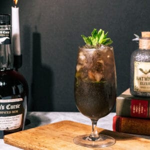 Mojito on a wood surface with a bottle of rum and a lit candle in the background.