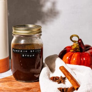 Jar of the pumpkin spice simple syrup with spices, a kitchen towel, and a decorative pumpkin next to it.