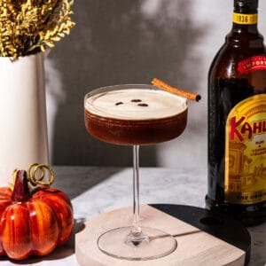 Pumpkin spice espresso martini with a pumpkin, flowers, and a bottle of Kahlua in the background.