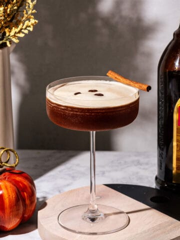 Pumpkin spice espresso martini with a pumpkin, flowers, and a bottle of Kahlua in the background.