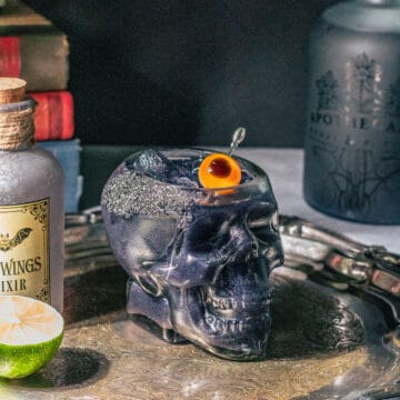 Black Magic Margarita in a skull cocktail glass with books and apothecary bottles around it.