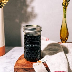 Jar of the syrup on a wood surface with flower in a vase.