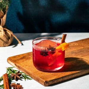 Christmas negroni sitting on a wood surface with a dark blue background.
