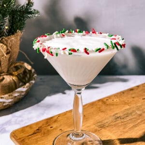 Sugar cookie martini on a wood surface with a Christmas tree in the background.