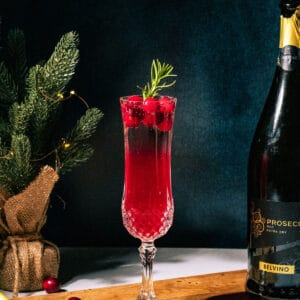 Poinsettia mimosa on a wood surface with a mini Christmas tree and bottle of prosecco in the background.