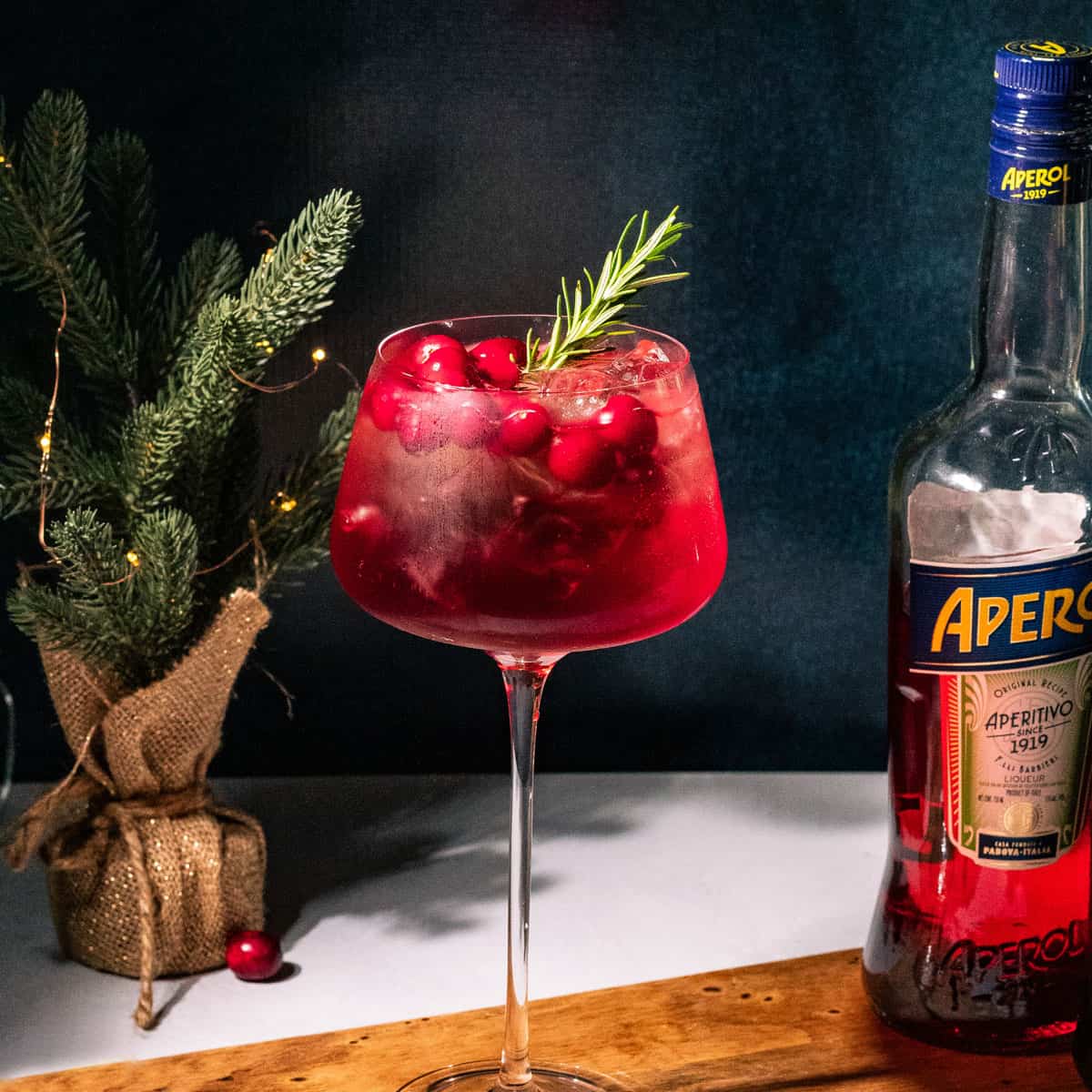 Spritz on a wood board with a mini Christmas tree and bottle of Aperol in the background.