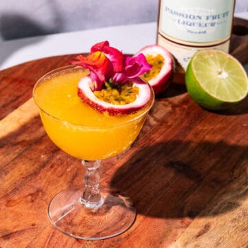 Passion fruit martini garnished with a floating passion fruit half and edible flowers.