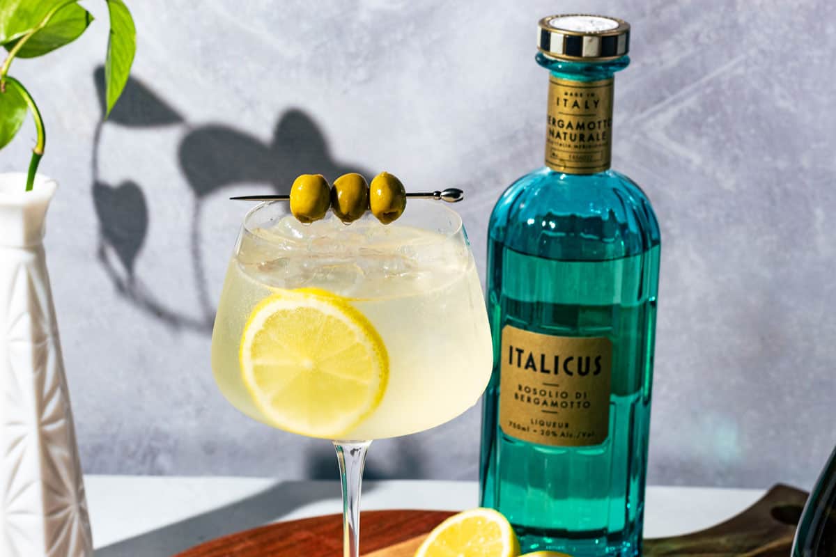 The spritz garnished with green olives and a lemon slice with a bottle of Italicus behind it.