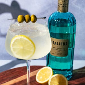 Italicus spritz on a wood surface with the bottle and lemon halves in the background.