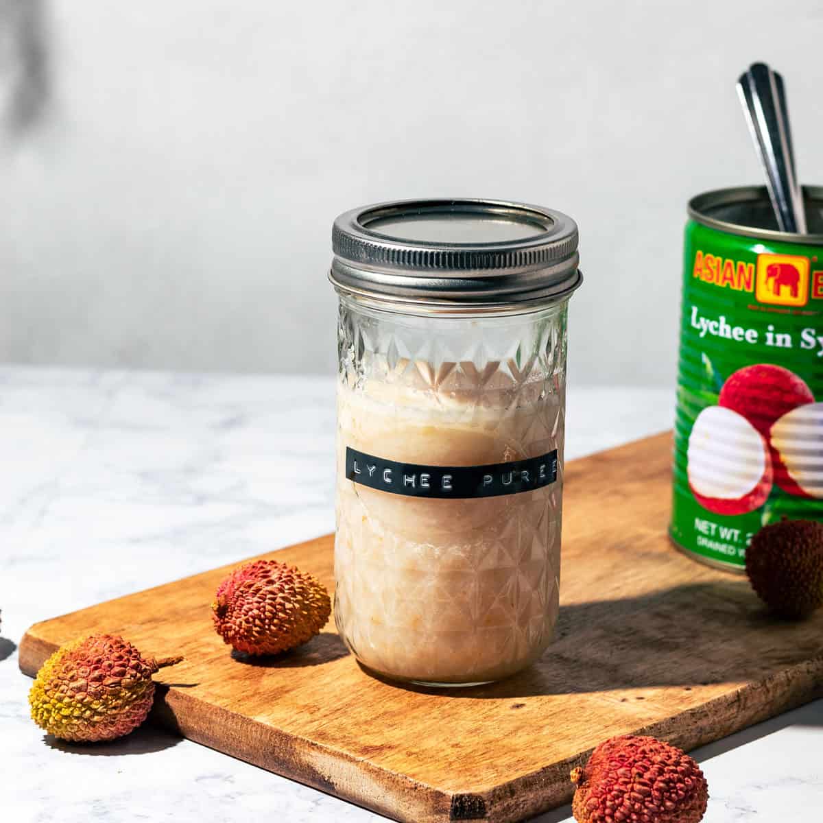 Mason jar of lychee puree on a wood cutting board.