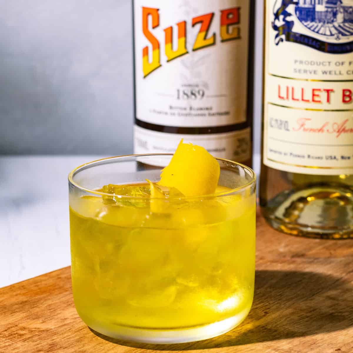 The cocktail on a wood surface with a bottle of Salers and Lillet Blanc in the background.