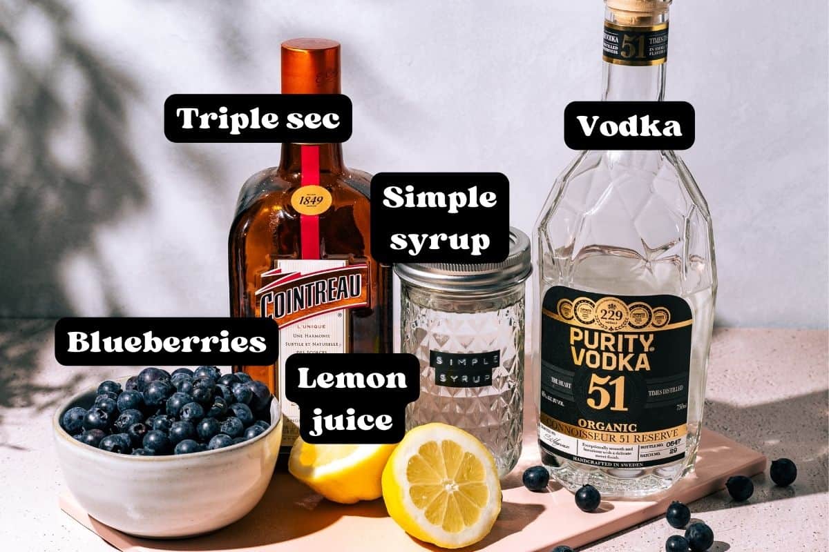 Ingredients for the cocktail spread out on a pink surface.