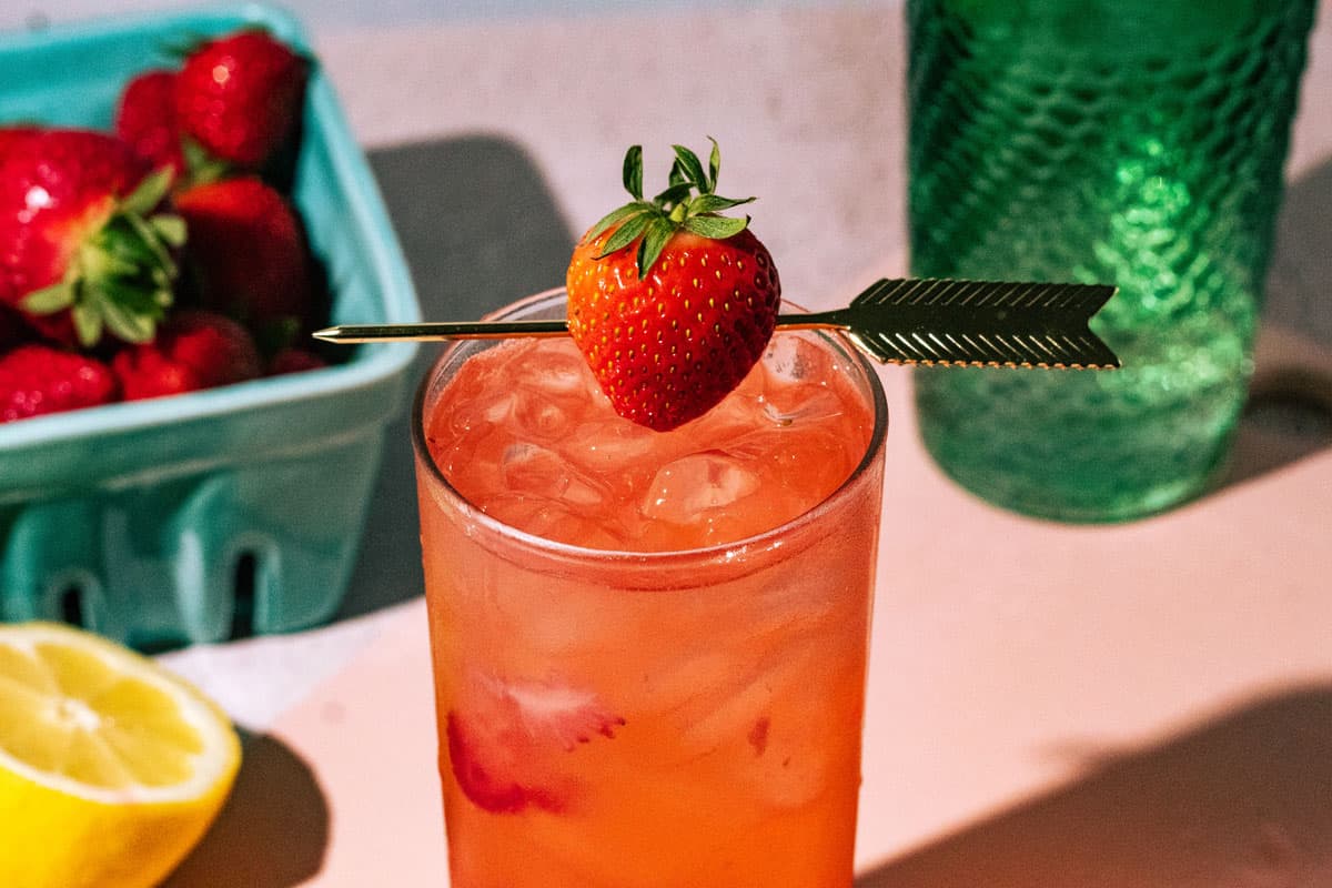 Fresh strawberry on a cocktail pick garnishing the gin and tonic.