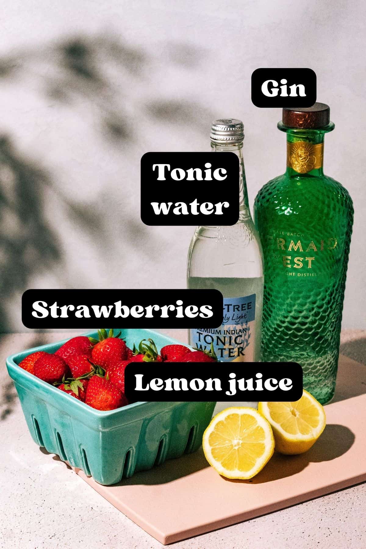 Ingredients for the cocktail spread out on a pink surface.