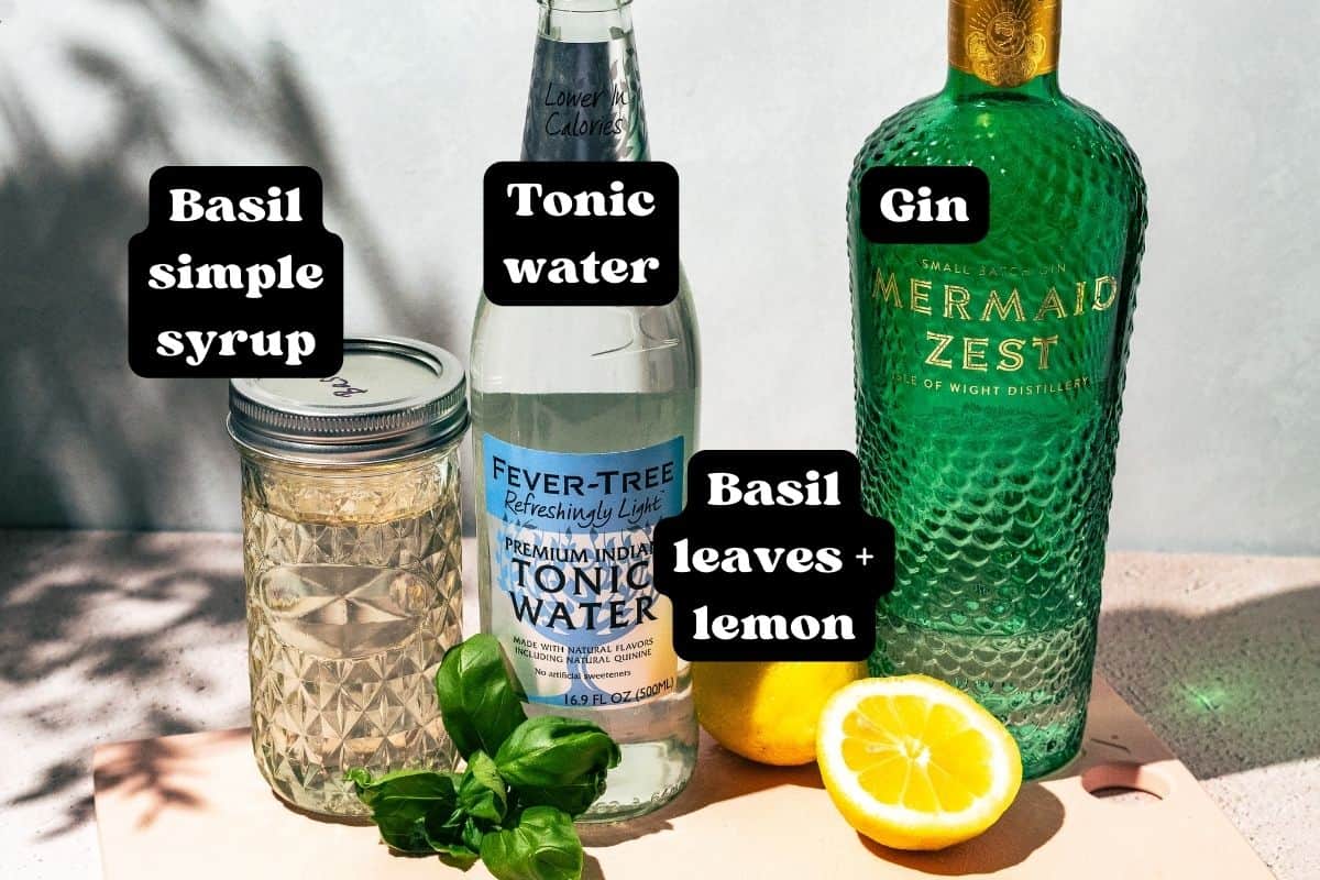 Ingredients for the cocktail spread out on a pink surface.