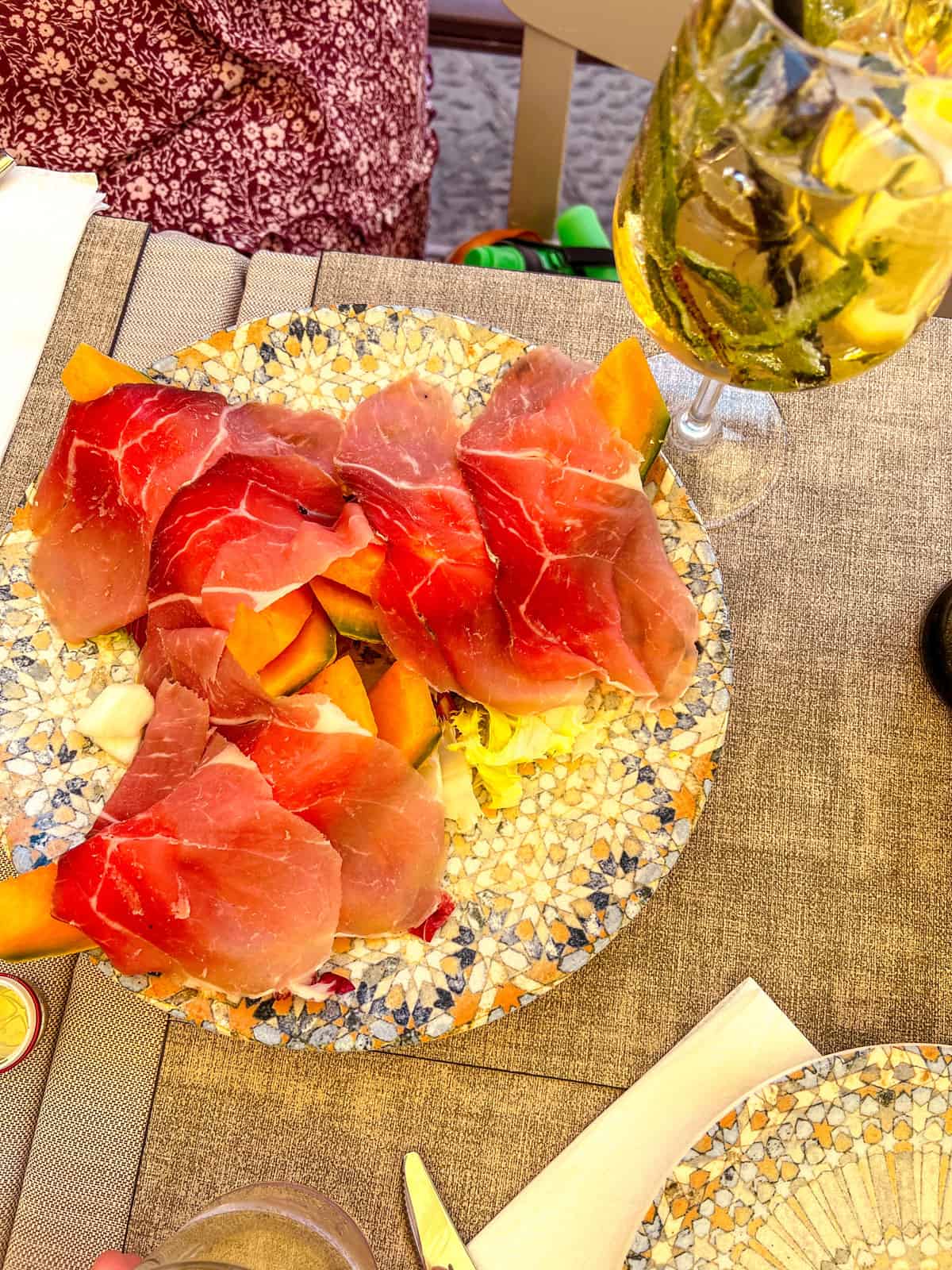 Platter of melon and prosciutto next to a Hugo Spritz.