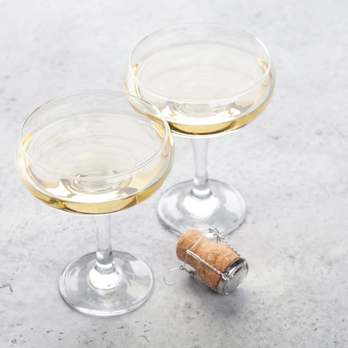 Two glasses of sparkling wine with a cork on the side.