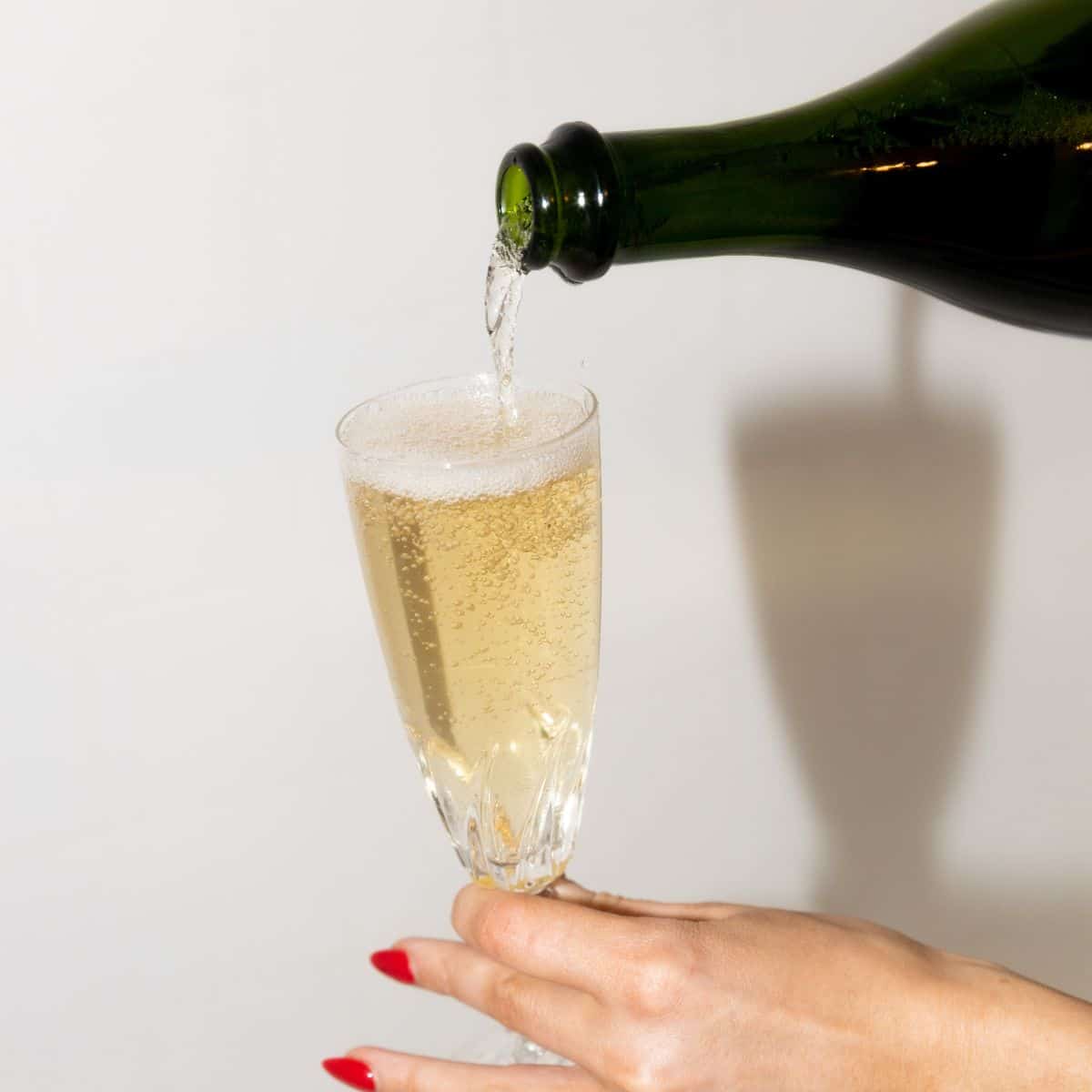 Sparkling wine being poured into a champagne flute with someone holding the stem.