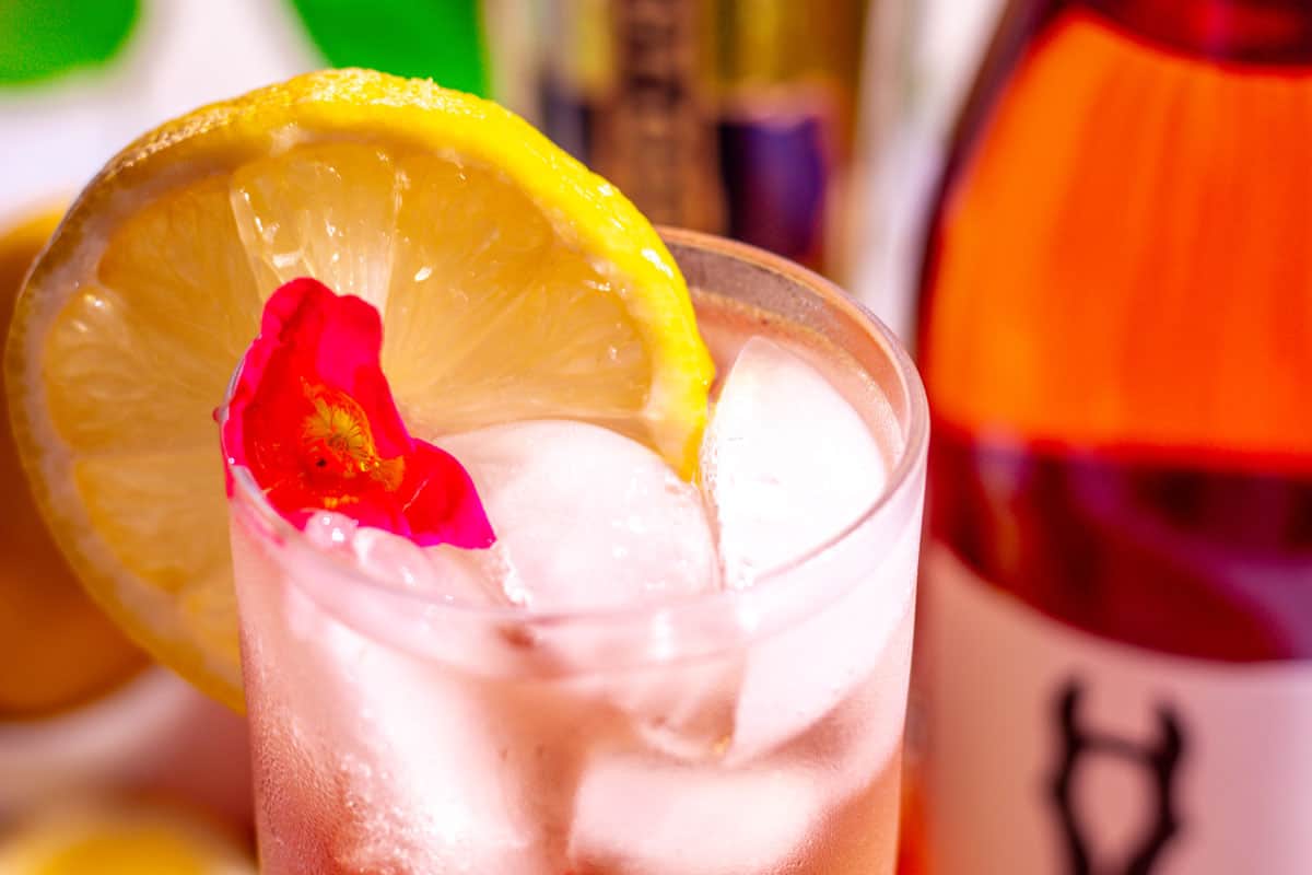 Lemon and a pink edible flower garnishing the cocktail.