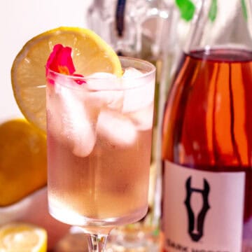 Wine spritzer on a wood surface with a bottle of rosé wine in the background.