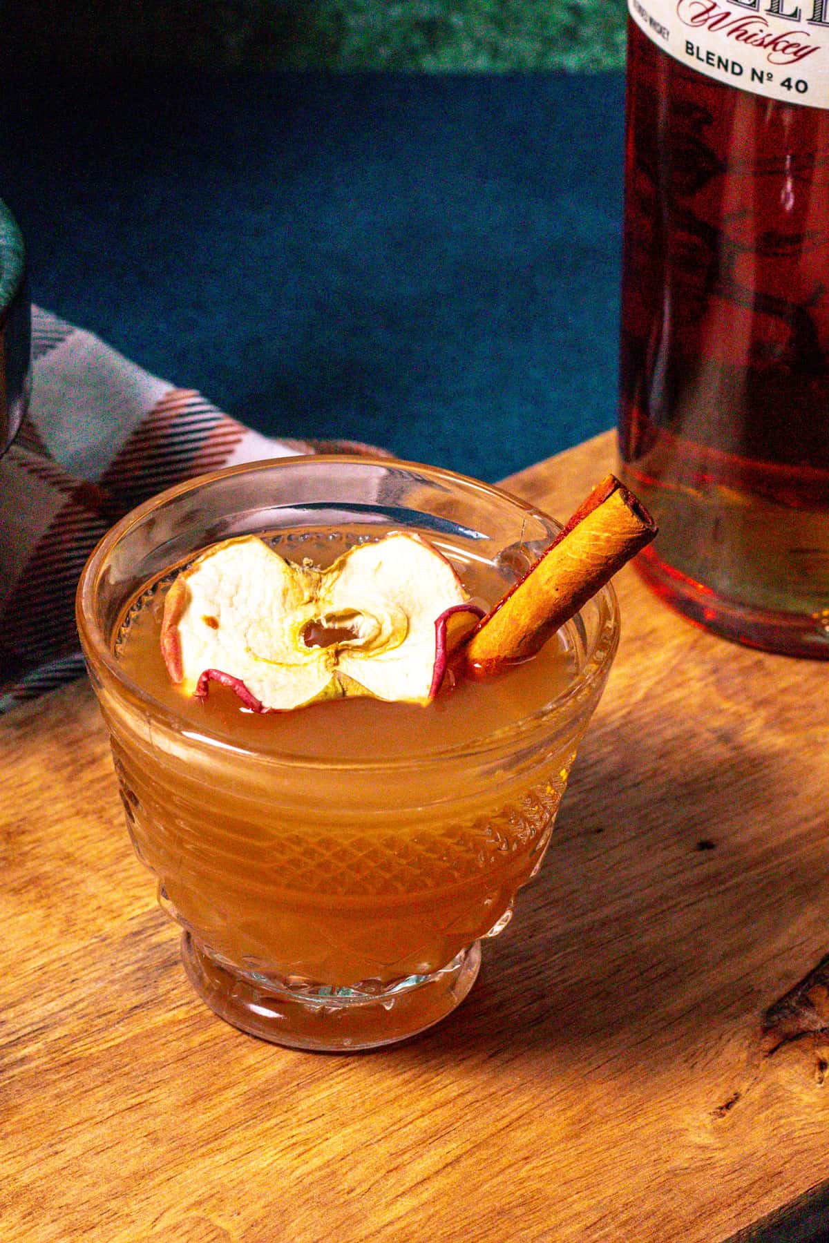 Hot toddy on a wood surface garnished with a dried apple slice and cinnamon stick.