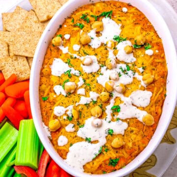 The dip in a white dish surrounded by veggies and crackers.