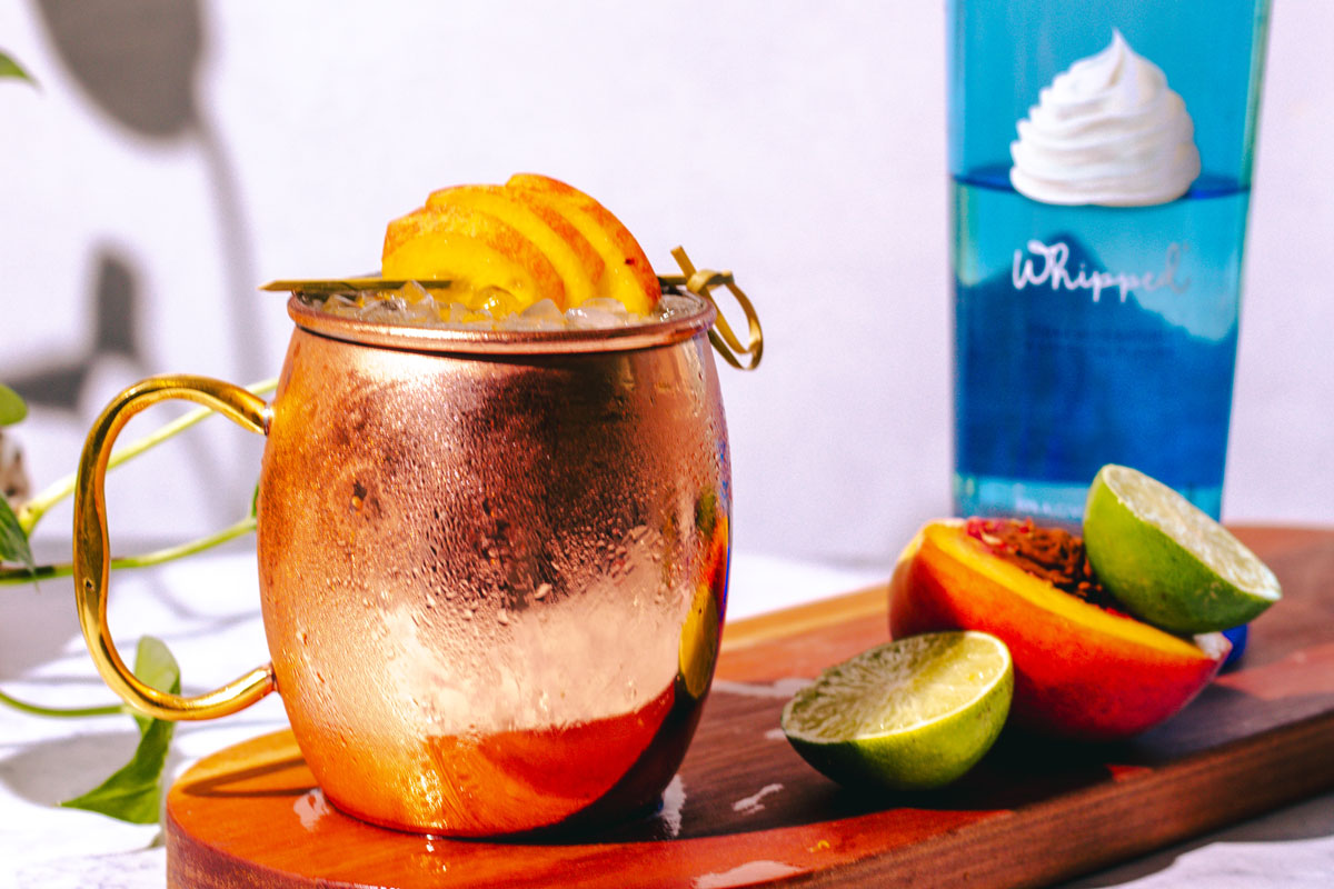 Moscow Mule on a wood surface with peaches and limes on the side.