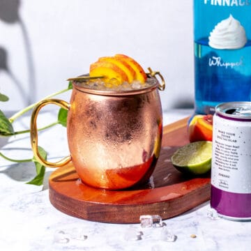 Moscow mule in a copper mug garnished with peaches.