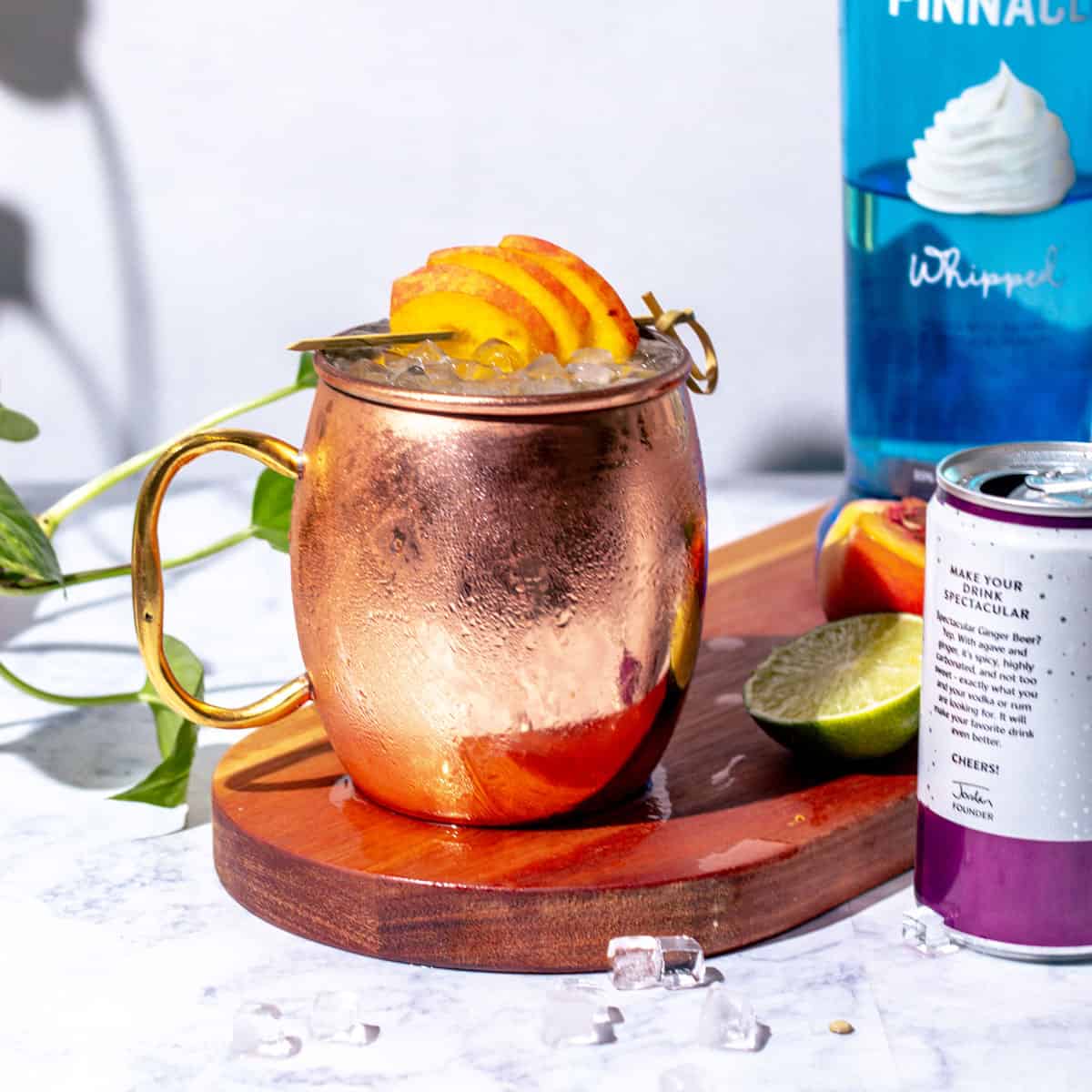 Moscow mule in a copper mug garnished with peaches.